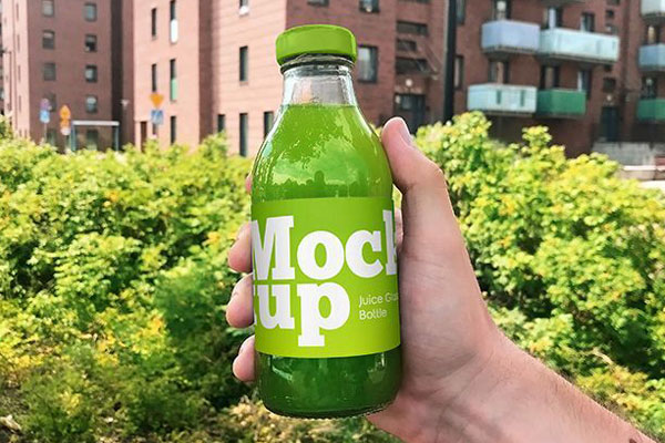 Front View of a Juice Glass Bottle Held Up by a Hand Mockup