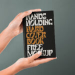 Front View of Hand Holding Hardcover Book Mockup