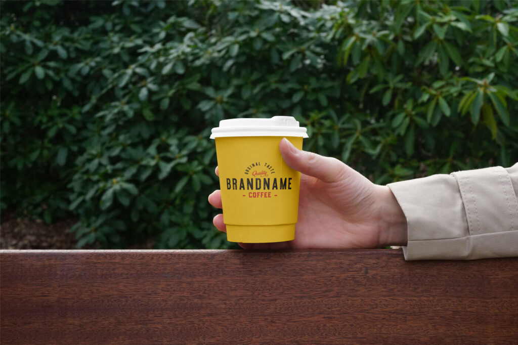 Hand Holding Paper Coffee Cup on Bench Mockup