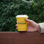 Hand Holding Paper Coffee Cup on Bench Mockup