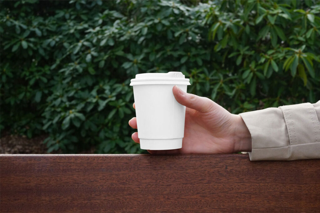 Hand Holding Paper Coffee Cup on Bench Mockup