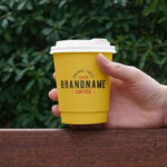 Hand Holding Paper Coffee Cup on Bench Mockup