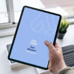 Mockup Showcasing Hand Holding iPad in a Office Table Scene